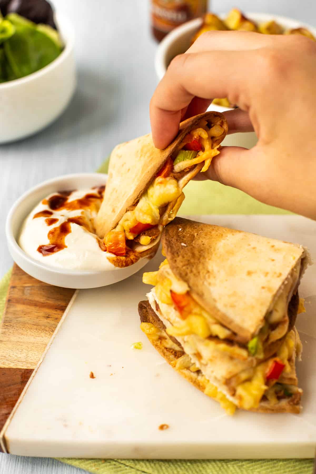 A hand dipping a piece of quesadilla into a small bowl of sour cream.