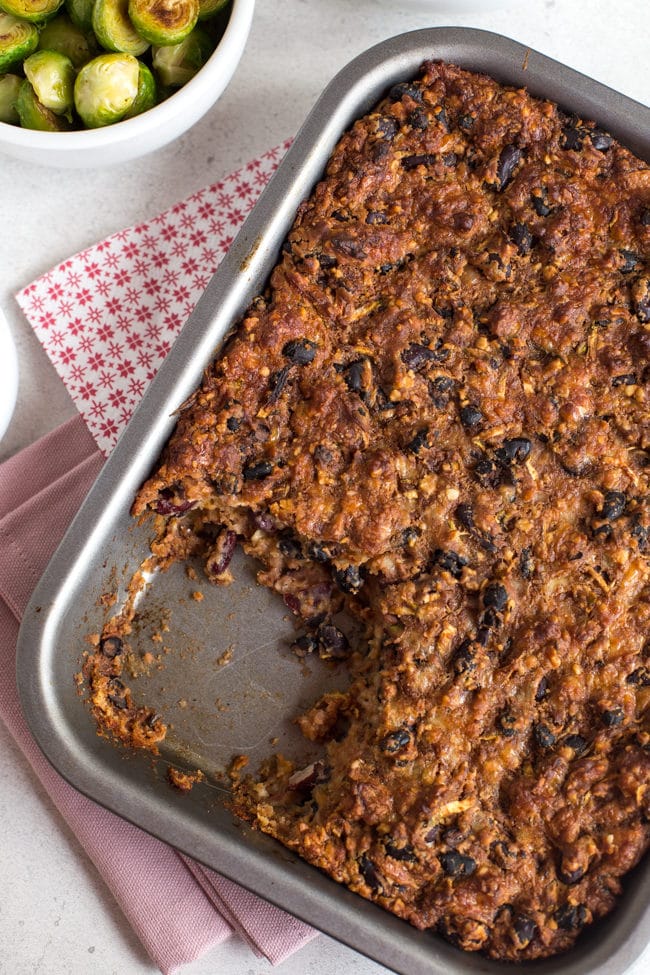 A cheesy bean roast in a baking dish with a large spoonful removed.