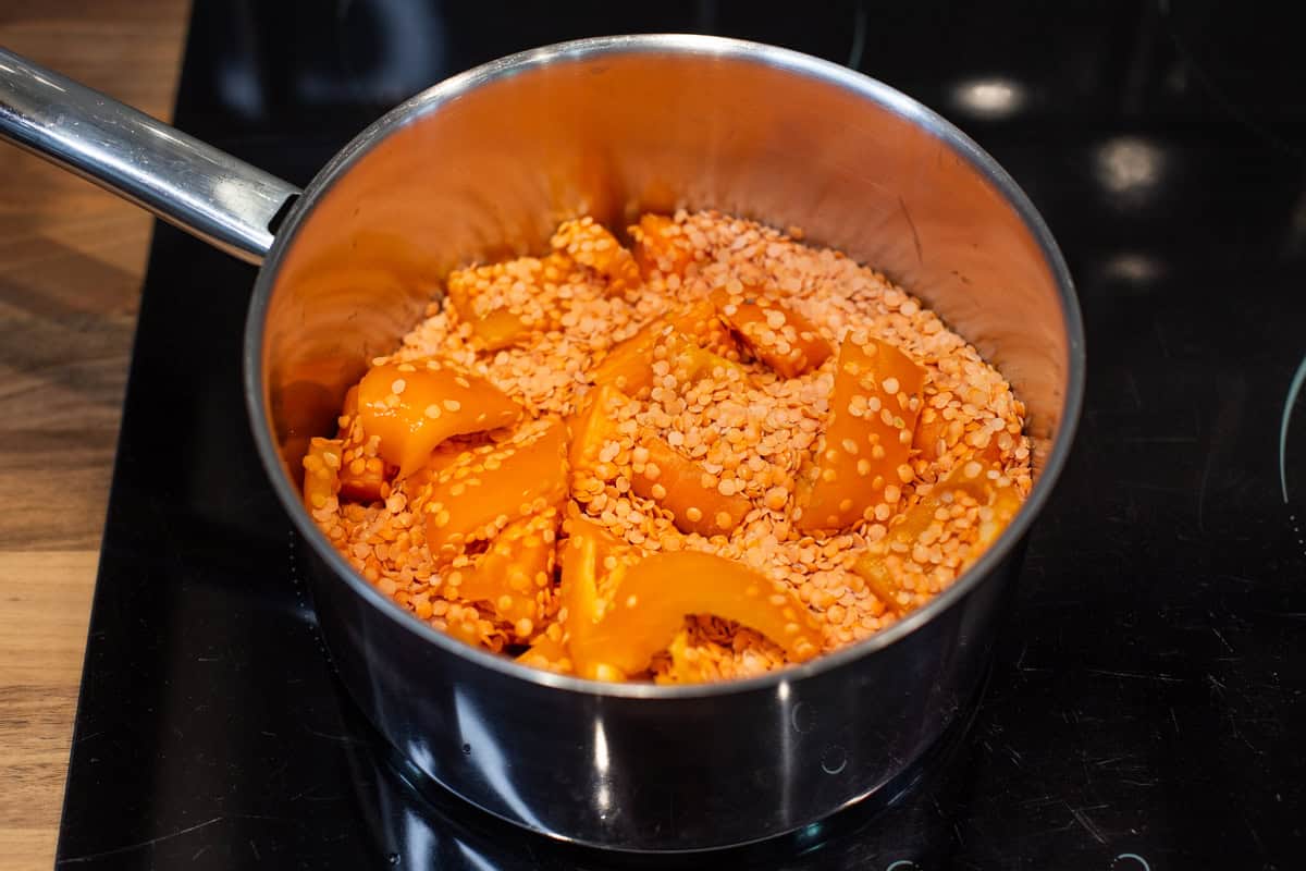 Uncooked red lentils and vegetables in a saucepan.