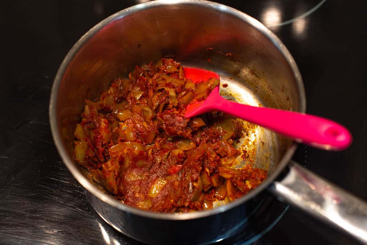 Onion, spices and tomato puree cooking in a saucepan.