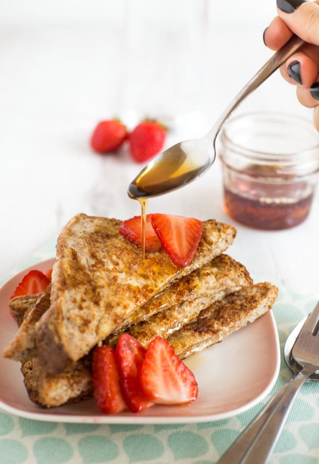 A hand drizzling syrup onto a stack of wholewheat French toast.