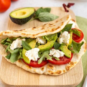 A homemade flatbread on a board, stuffed with avocado, tomatoes and fresh mozzarella cheese.