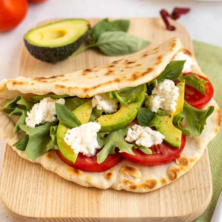 A homemade flatbread on a board, stuffed with avocado, tomatoes and fresh mozzarella cheese.