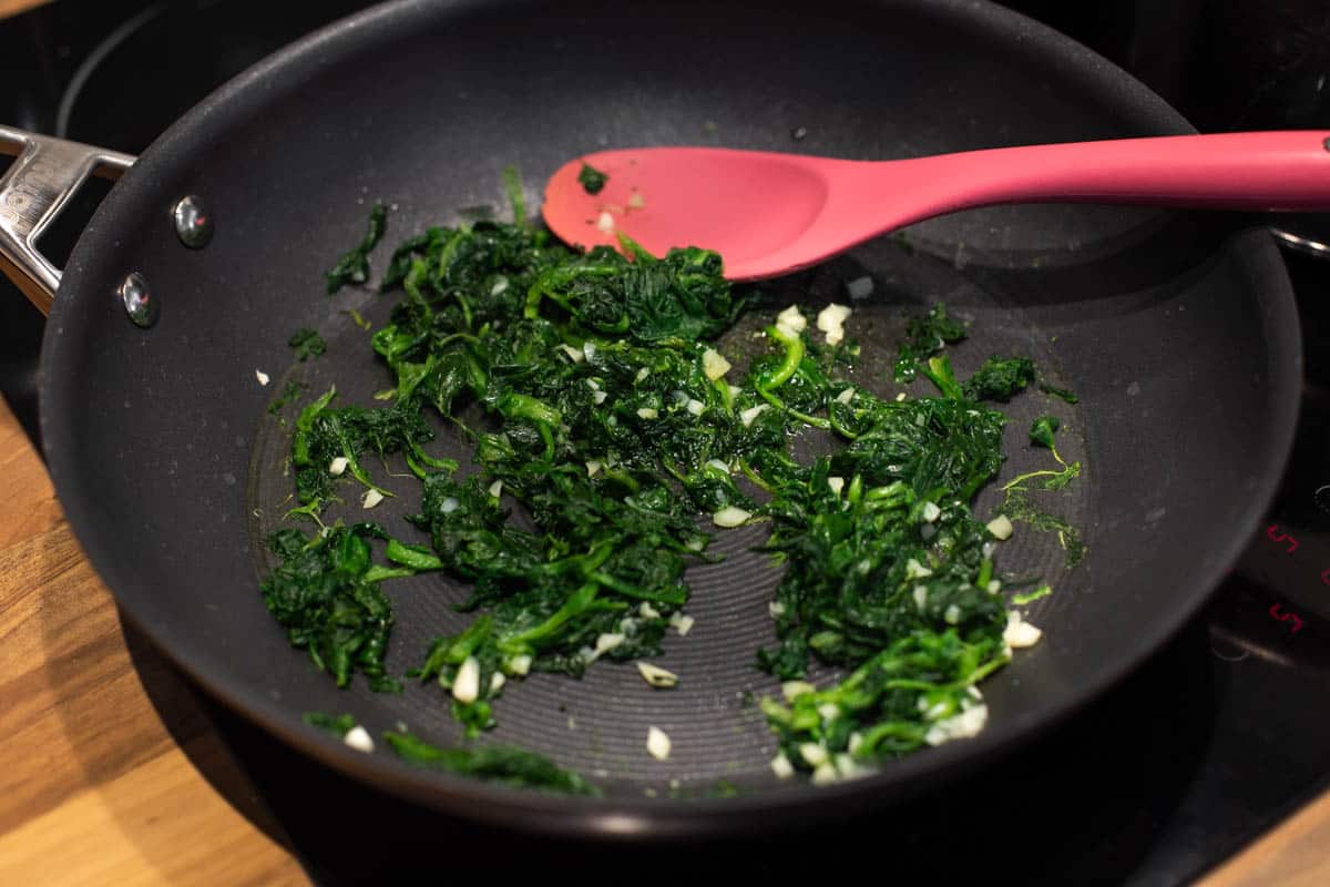 Frozen spinach being sautéed in a frying pan.