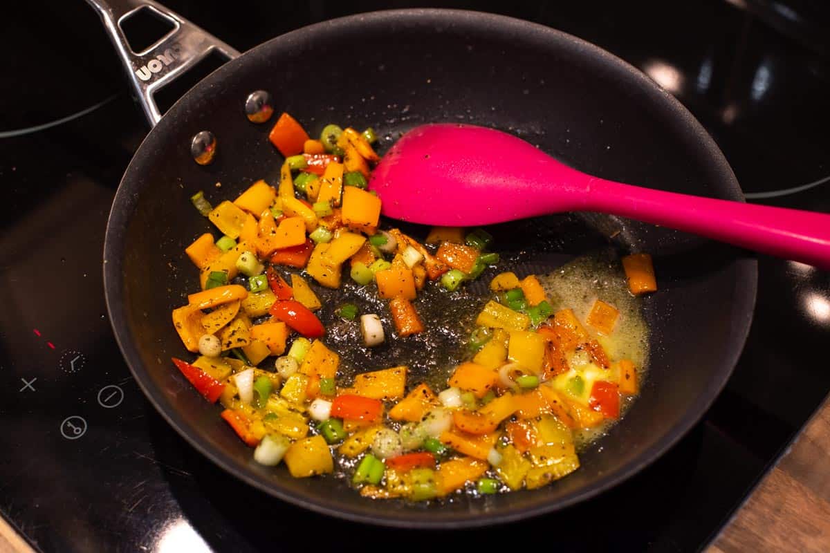 Peppers and spring onions cooking in a frying pan.