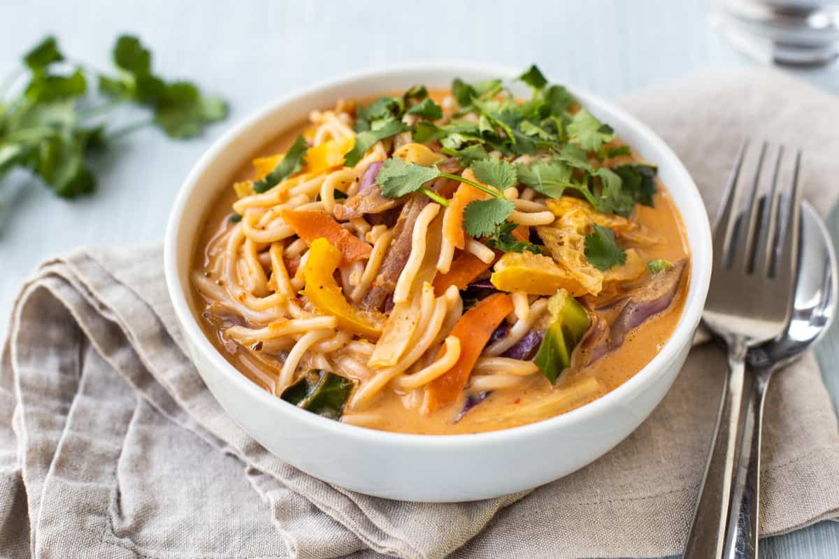 A bowlful of red Thai curry noodle soup with a napkin and cutlery.