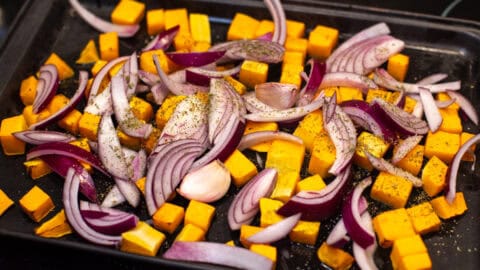 Diced butternut squash and red onion on a baking tray.
