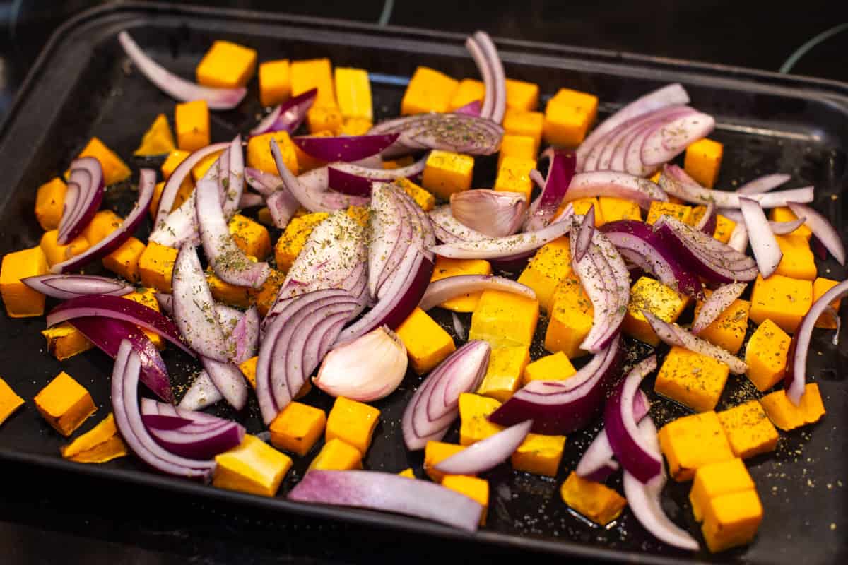 Diced butternut squash and red onion on a baking tray.