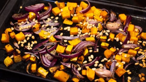 Roasted butternut squash, red onion and pine nuts on a baking tray.