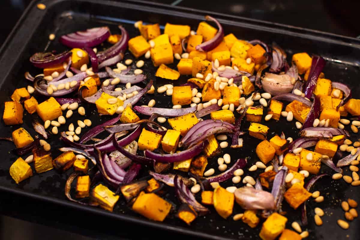 Roasted butternut squash, red onion and pine nuts on a baking tray.