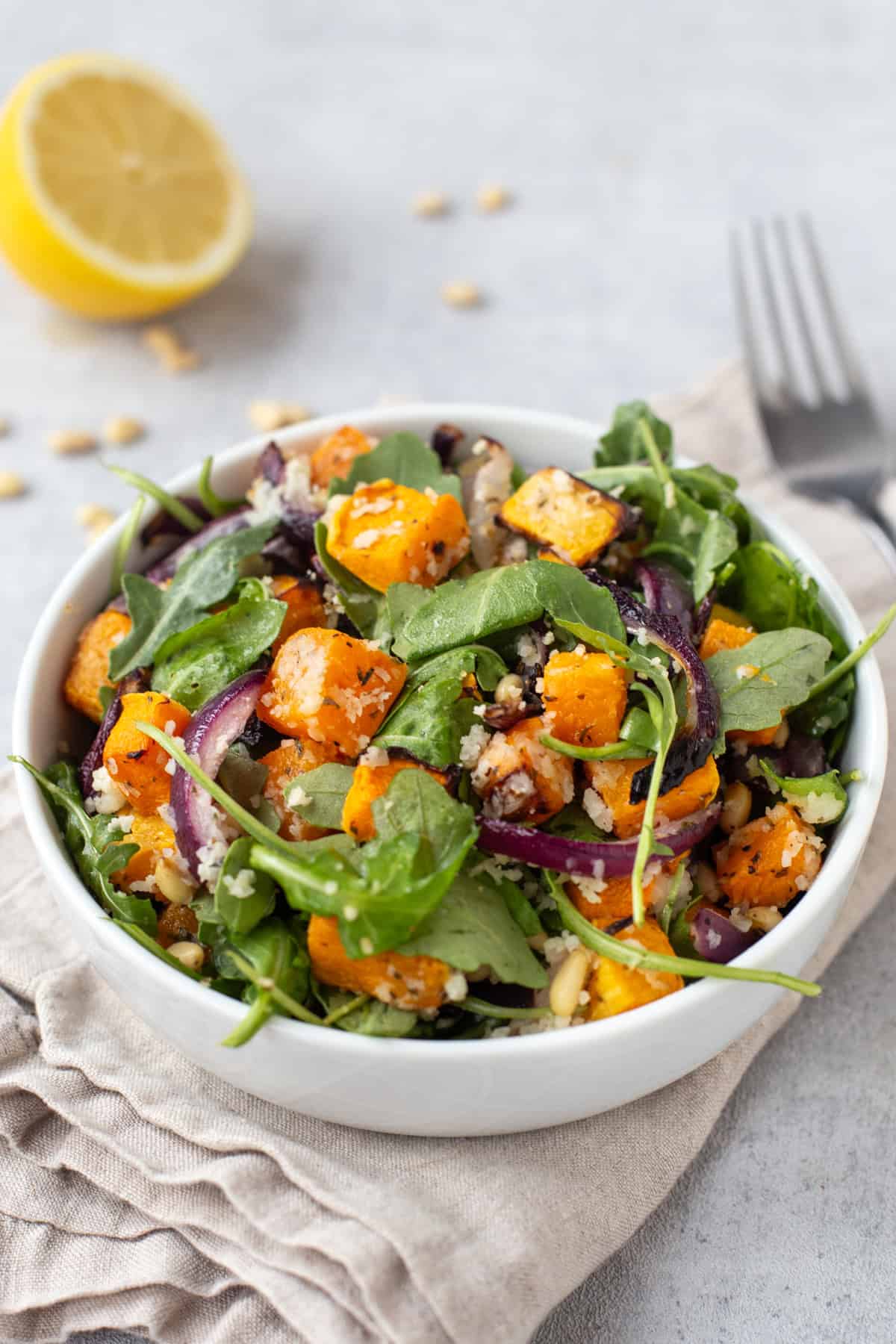 A portion of roasted butternut squash salad in a bowl with red onion and arugula.