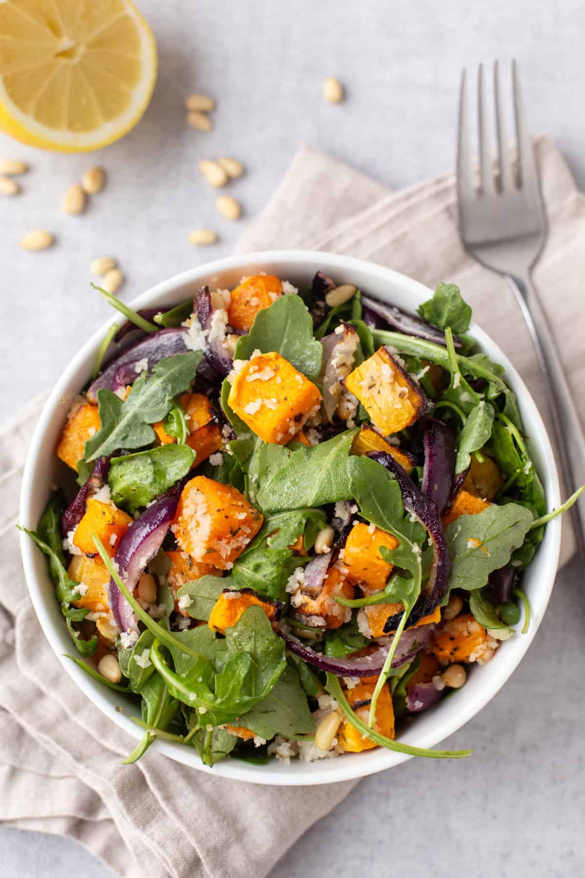 Overhead shot of a portion of roasted butternut squash salad in a bowl with red onion and arugula.