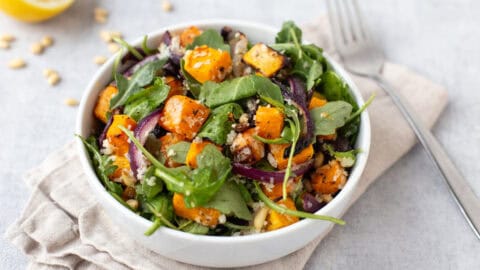 A portion of roasted butternut squash salad in a bowl with red onion and arugula and goat cheese.