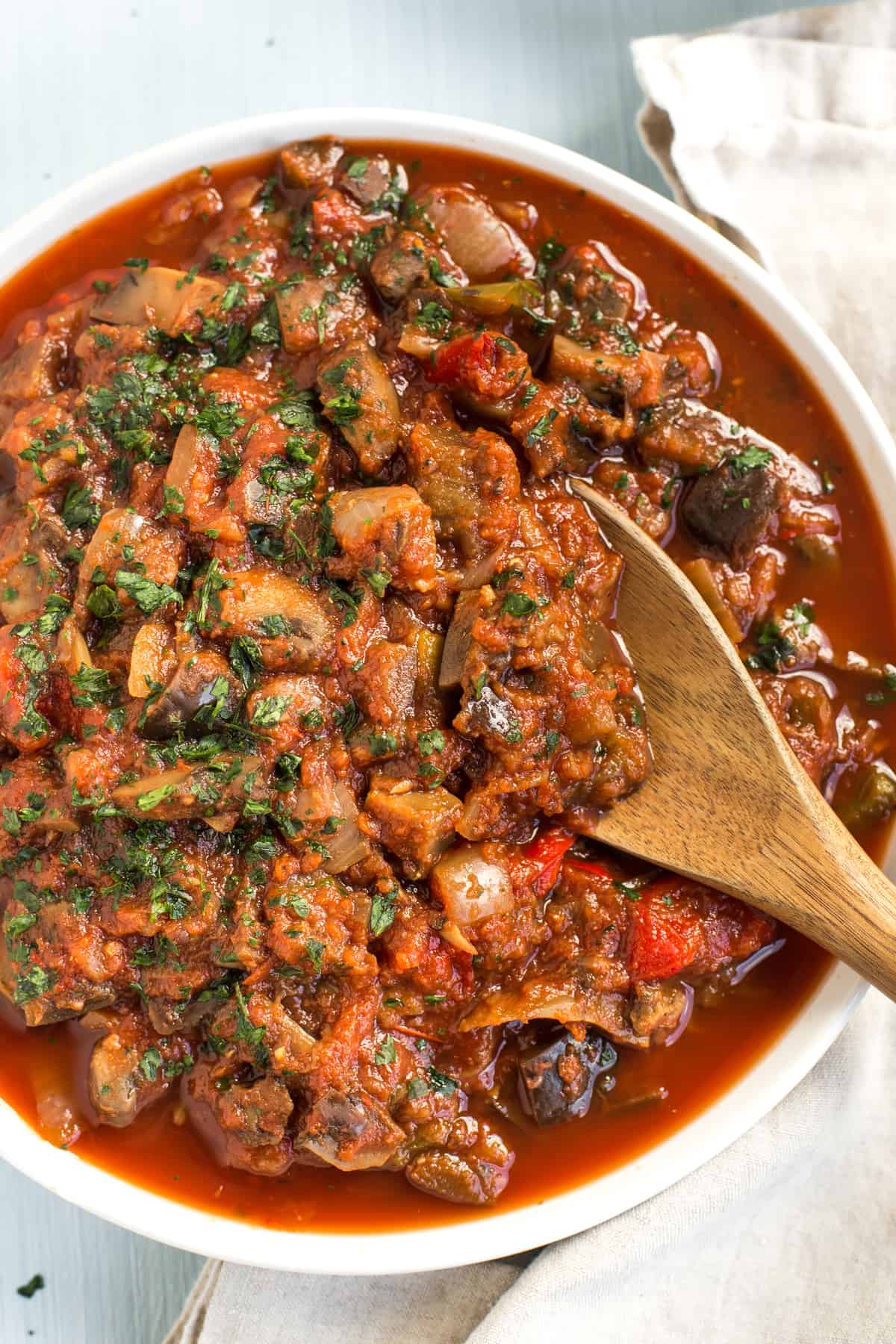 Overhead shot of a rich vegetable ratatouille in a bowl being scooped with a wooden spoon.