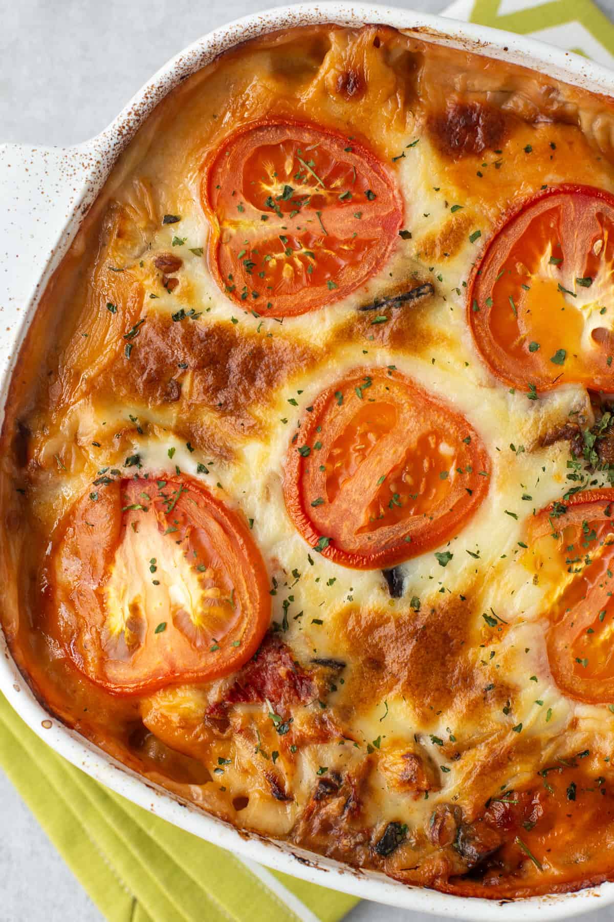 Overhead shot of a cheesy topped moussaka casserole with sliced tomatoes.